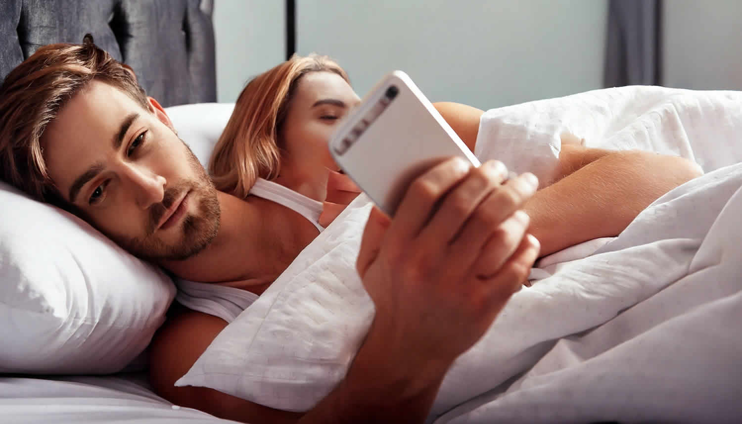 Infidelity Investigation - couple in bed - man secretly texting